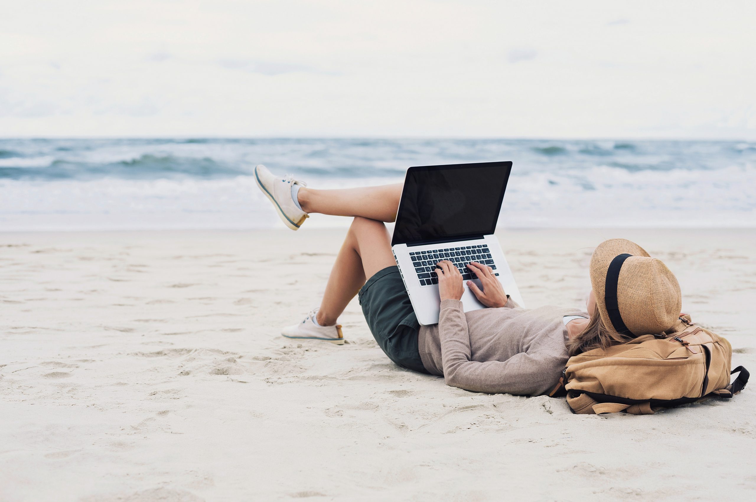 旅をしながらビーチでノートパソコンを操作する男性